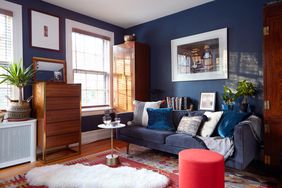 den with deep navy walls; navy low-back sofa; warm wood cabinet and red/blue rug