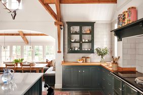 Kitchen with rich green cabinetry, minimal upper cabinets, cream colored wall tiles, rustic beam vaulted ceiling, and tiled floors