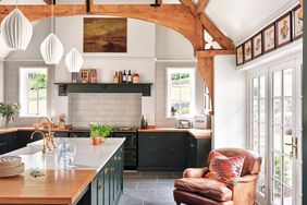 English Kitchen with rustic beamed vaulted ceiling, rich green cabinetry, cream colored wall tile, gray tile floors and butcher block countertops