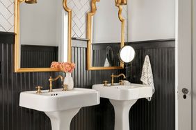 two pedestal sinks and two gold mirrors in bathroom with tile floor