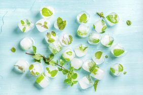 Ice cubes with frozen mint leaves inside on blue background