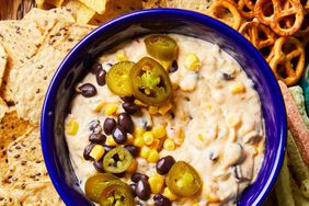 Hot corn dip in blue bowl surrounded by snacks