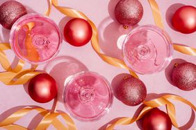 Pink cocktail glasses surrounded by ornaments and ribbon on pink background