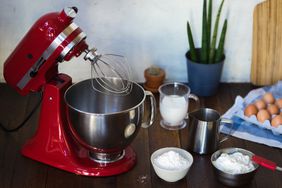 Red stand mixer on wooden table with baking ingredients