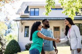 Couple meeting with real estate agent in front of home