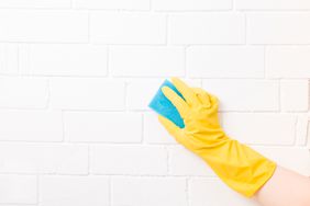 hand with rubber gloves and sponge cleaning wall