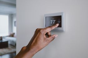 hand adjusting thermostat temperature in home