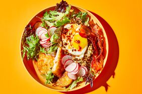 a yellow bowl filled with greens, an egg, strips of bacon, and sliced radishes