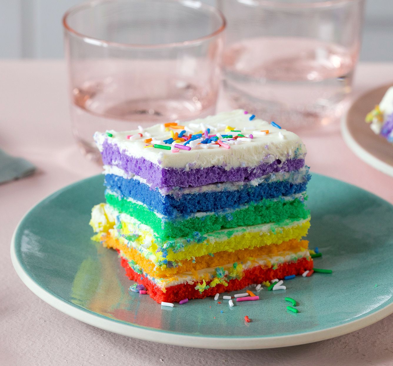 rainbow layered cake with white icing and sprinkles