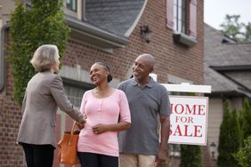 Real Estate Agent shaking hands with smiling couple outside house for sale