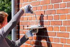 bricklayer cementing repairs on exterior house wall 